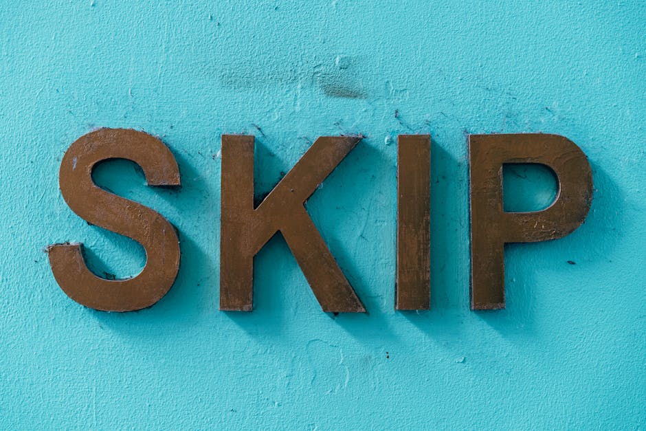 A close-up of three large, individual metal letters spelling 'SKIP' mounted on a textured light blue wall. The letters are dark brown with a slightly rough, matte finish and are affixed directly to th